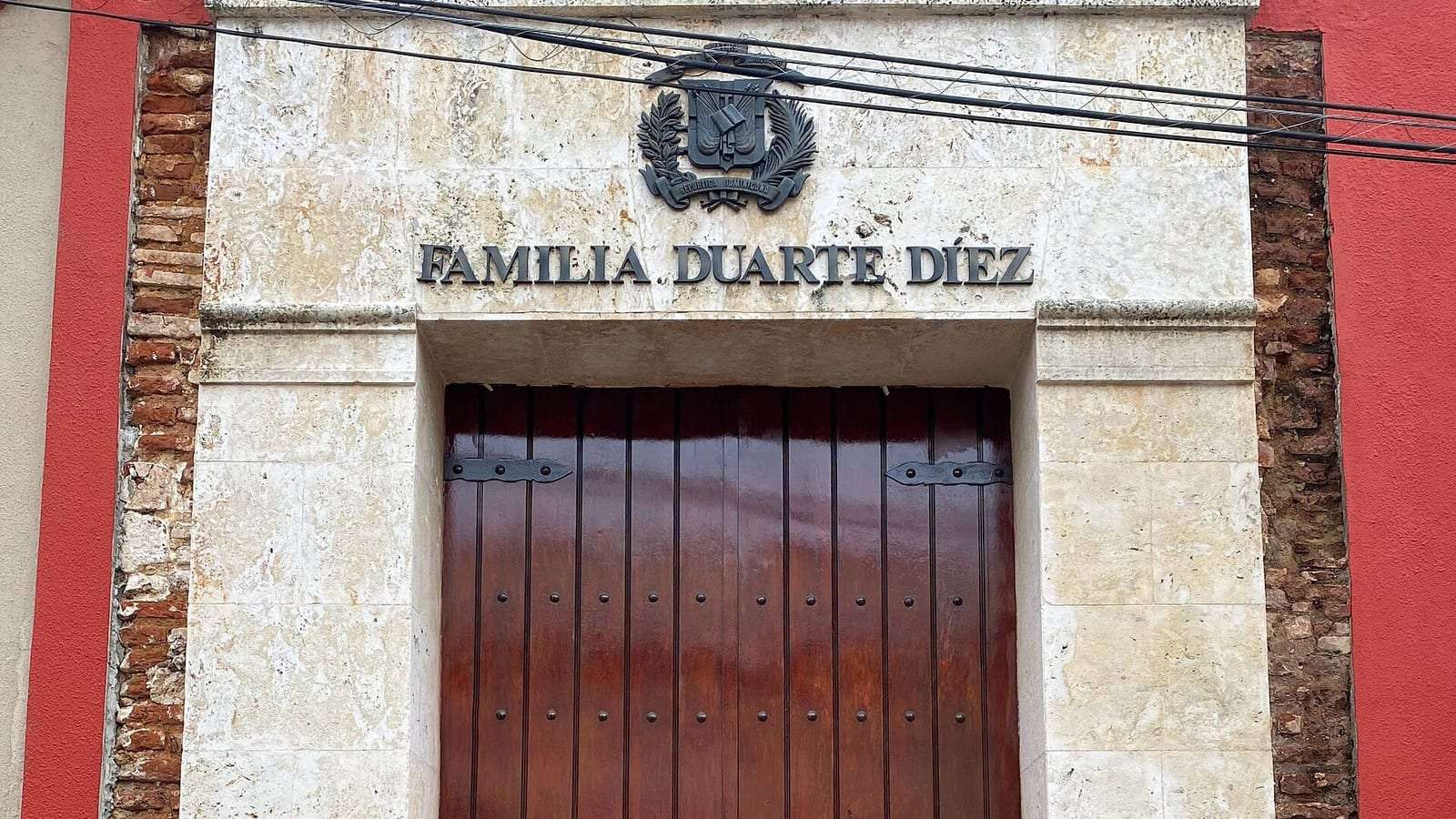Portada de piedra con puerta de madera y la inscripción «Familia Duarte Díez» bajo el escudo dominicano, en la fachada roja de la Casa de Duarte, en la Ciudad Colonial