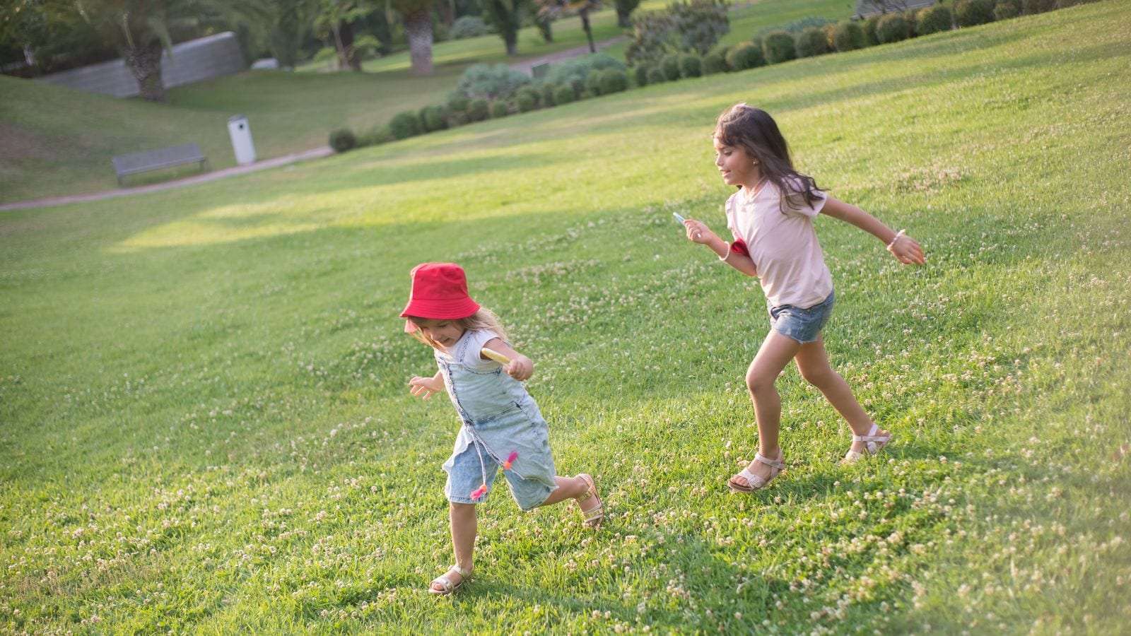 Dos niñas corren por una ladera de césped en un parque soleado