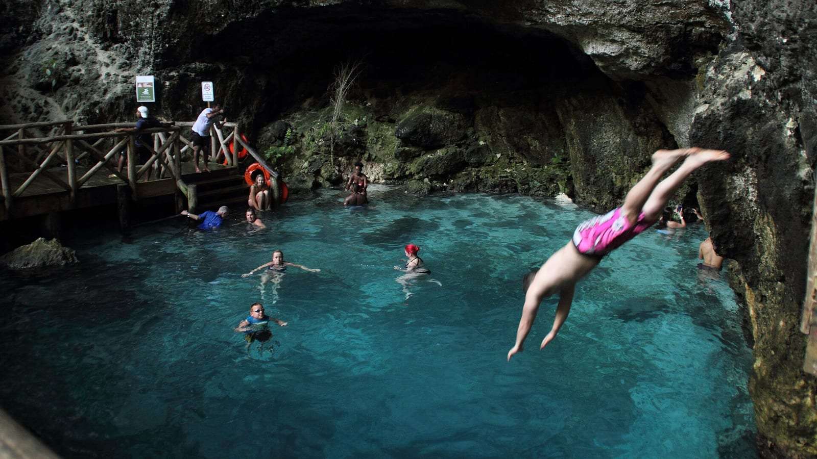 Bañistas en el agua turquesa del Hoyo Azul, una poza bajo la roca en Cap Cana, mientras alguien se lanza de cabeza